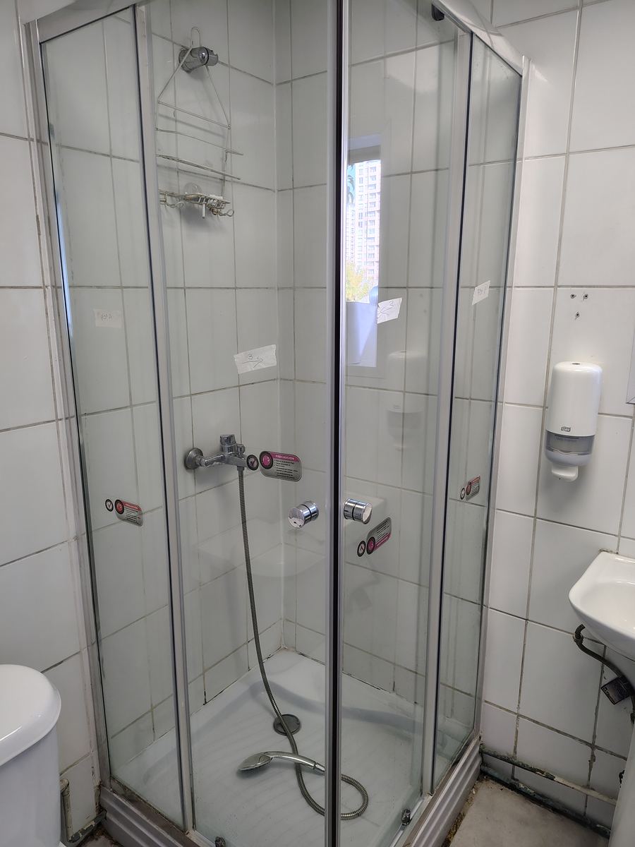 Ducha con mampara de vidrio antes de la intervención, con cintas de marcación en los paños