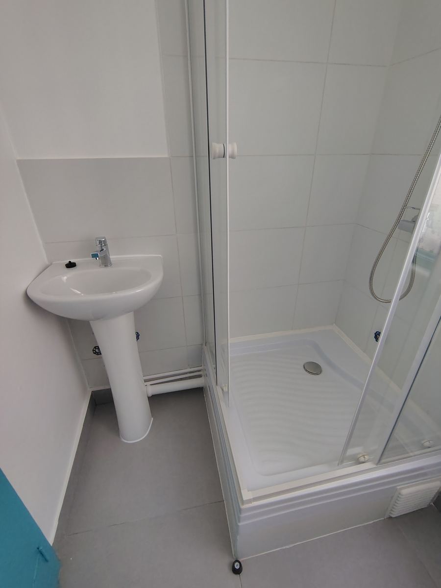Lavamanos y ducha del baño terminado, con los muros blancos